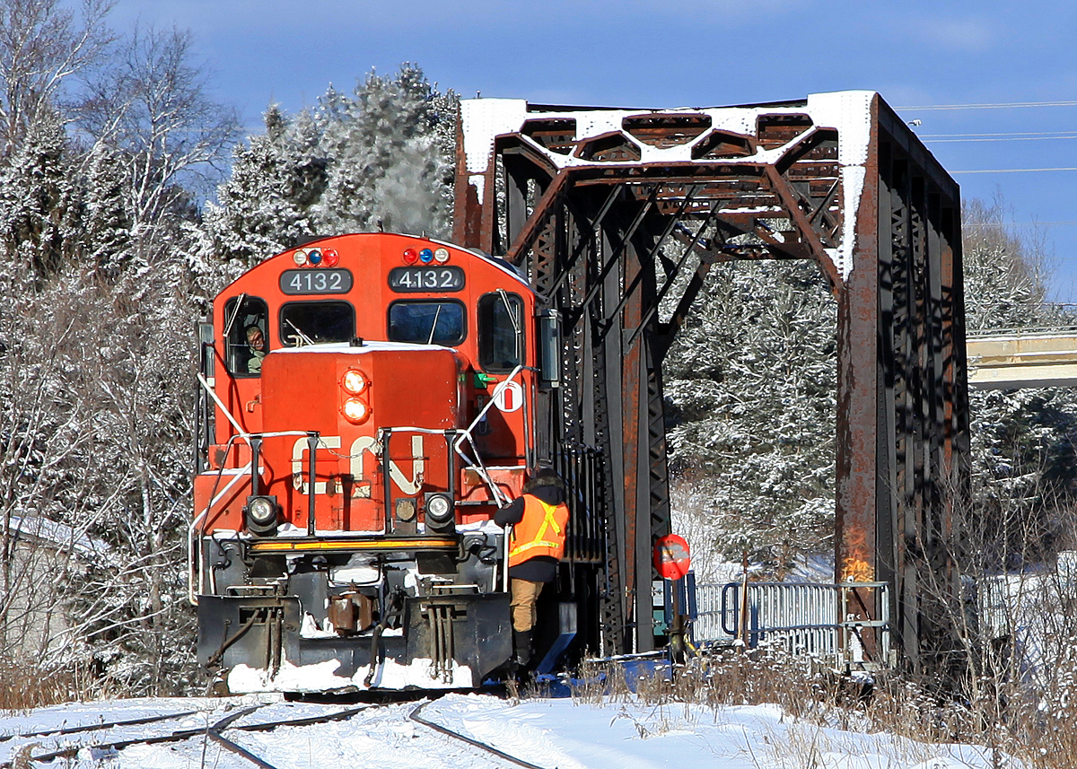 After dropping 6 cylindrical hoppers at the KWH Pipe plant at the north end of Huntsville Yard 4132 backs up to get back on the main so they can head back into the yard to finish up the switching they've been doing there all morning. The bridge in the background carries the CN Newmarket Sub over the Muskoka River northward to North Bay.