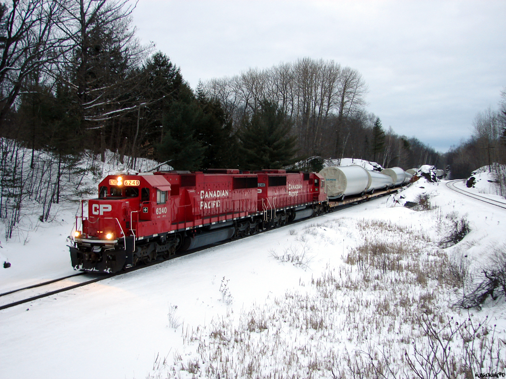 CP 6240 South with train DIM-006 very slowly pull through Rosseau Road on the approach to Brignall, these W10 dimensional loads had a stop, examine, and proceed at 3 MPH restriction through the rock-cuts pictured in the background. Pictured here at 16:42, the pressure was on with 12 miles to go before getting into MacTier to tie down in track 2 for the night, as these loads are restricted to daylight movement only unless special authorization.