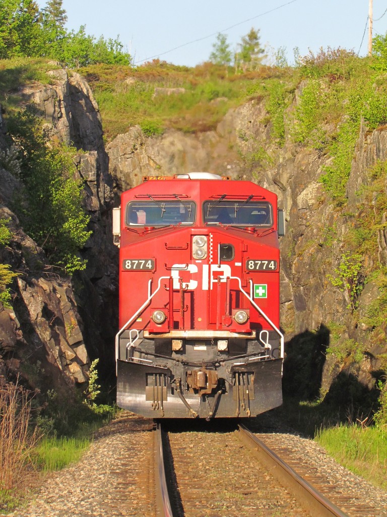 A little over a mile to the west of the Kenora station the double track mainline splits with the south track boring straight through a rock knoll and the north track curving around it. Eastbound train cp110 running today with ES44AC CP8774 as the rear remote is about to pass through this short tunnel highlited with spring greenery.