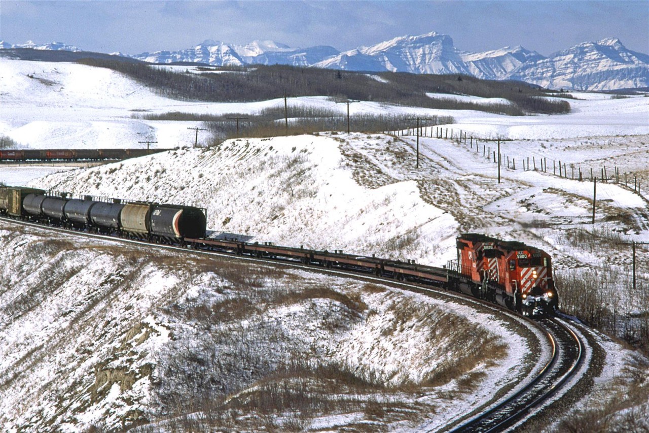 An eastbound manifest approaches the what was Glenbow siding, east of Cochrane. It was a nice clear day and the mountains and local area are covered with fresh snow.  I am not so sure that having 4 empty flat cars right behind the engines is such a good idea, even if the following hoppers are also empty, but I might be wrong.