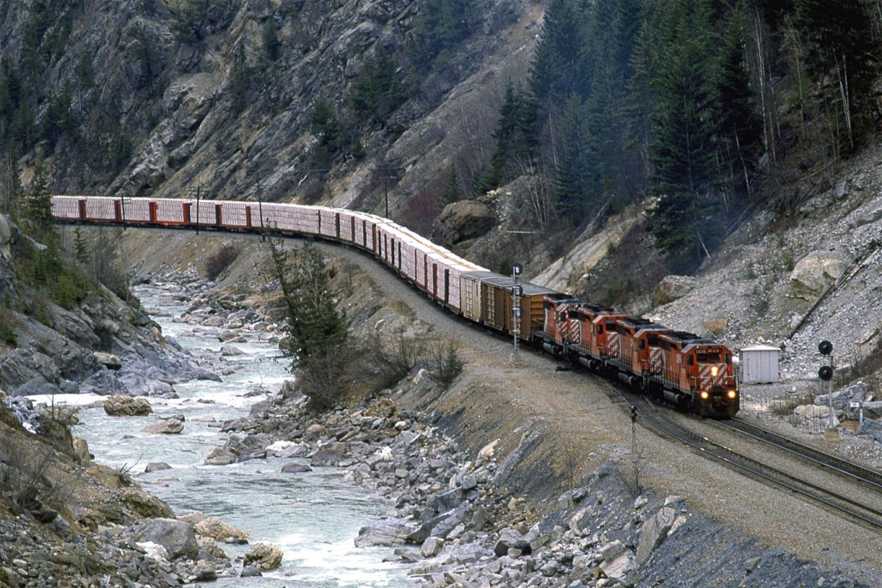 An eastbound wood products train is at the west switch of Glenogle, a few miles east of Golden BC. Water levels in the Kicking Horse River are still quite low, an indication that not much snow is melting in mid April.