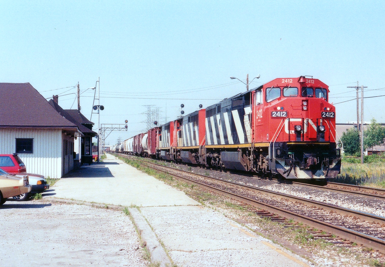 With a potential 12000 HP up front, a trio of nearly new Dash 8s are seen heading east on the Oakville  Sub rather than going up the Halton,  a rather uncommon practice in todays world. CN 2412, 2401 and 2425 provide the power. On the left, the old buildings are gone, the closest demolished and the other is CN Burlington West, since relocated, preserved, fronting nearby Fairview Av.