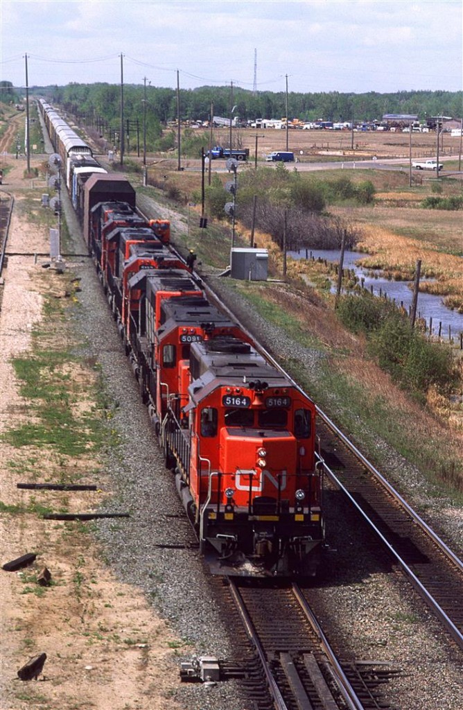 An eastbound auto train is approaching Edmonton. Note the beefy high railcar just behind the locomotives. It is there to clear ice from tunnels thus protecting the expensive automobiles following. Note the date.
A train with seven locomotives on the front end was very rare on CN. Typically, CN would run a train with only 2 engines on the mainlines in and out of Edmonton.