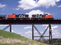 This is likely, but not necessarily an eastbound Clover Bar Transfer (Calder to Clover Bar Yard) beginning the crossing of the North Saskatchewan River in NE Edmonton.
The units are re-trucked GMD-1's. They were to become very common for switch in transfer duties in Edmonton. The need for the 1A1 trucks in the Edmonton area (and likely system wide) was diminishing at this time.
Those telegraph cable outriggers on the bridge would be removed sometime around 1991 when CN decides to rid the landscape of the poles and cables. 