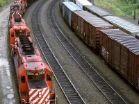 A coal train enters Revelstoke as a couple eastbound manifest trains, laden with wood products away their turn to make an assault on Rogers Pass.  