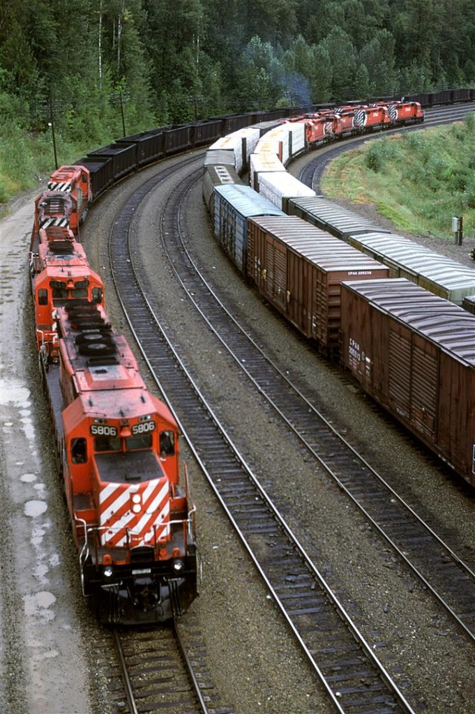 A coal train enters Revelstoke as a couple eastbound manifest trains, laden with wood products away their turn to make an assault on Rogers Pass.