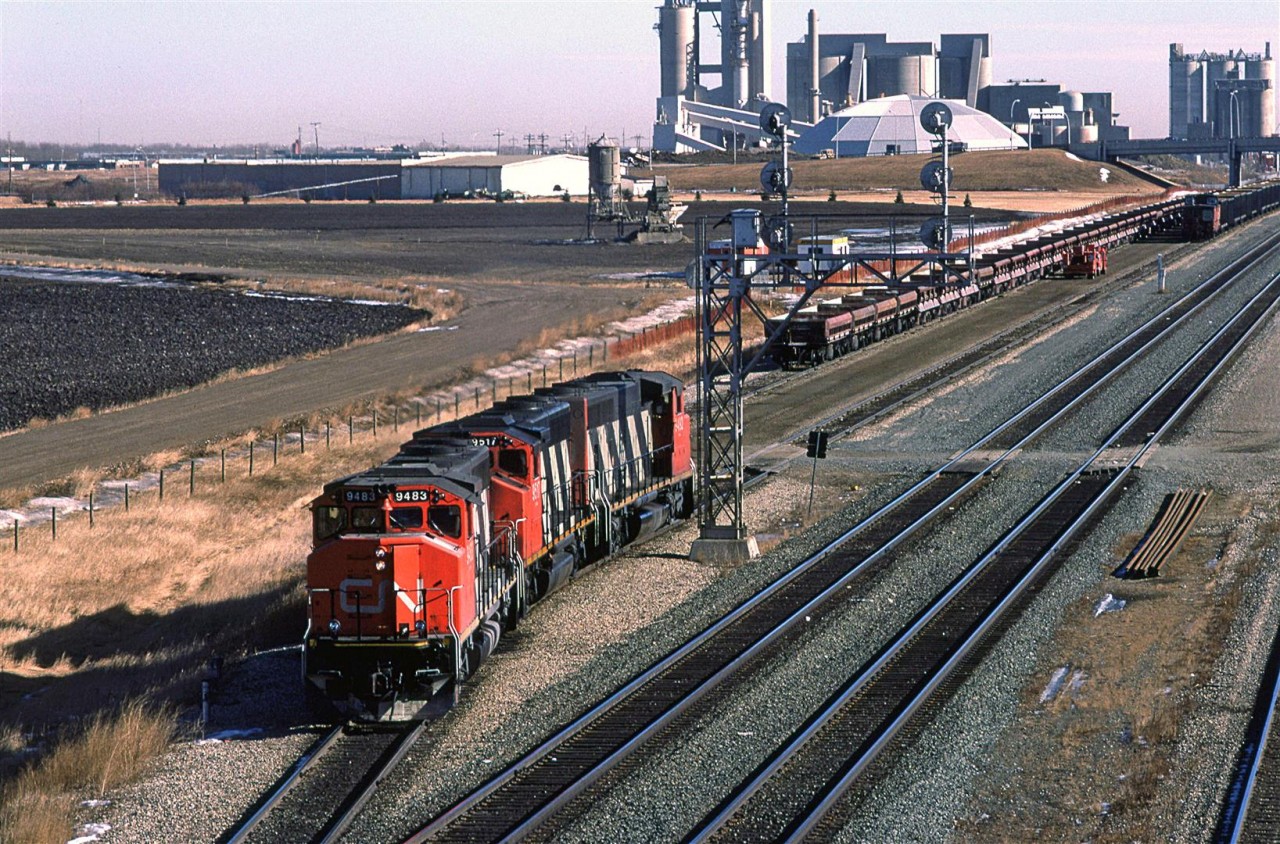 Something a little different today. We have 4-axle locomotives preparing to take a loaded sulphur train out of Edmonton. The sulphur train has a caboose on the west end. This is, in all likelihood, a train that loaded out on the western end of the Sangudo Sub (Kaybob, Benbow or Windfall). The Sangudo Sub leads face east as they enter the Edson Sub mainline, just beyond the Inland Cement plant in the background. Therefore, the loaded train arrived with the power on the east end as it entered town at Union Junction. It then backed onto Bissell yard.
The new power, seen here, will remove the caboose and place it on the west end of the aggregate train on the adjacent track. Then it will return to the sulphur cars, couple up, test, and leave for North Vancouver.