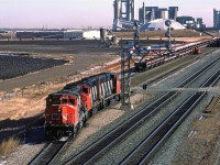 Something a little different today. We have 4-axle locomotives preparing to take a loaded sulphur train out of Edmonton. The sulphur train has a caboose on the west end. This is, in all likelihood, a train that loaded out on the western end of the Sangudo Sub (Kaybob, Benbow or Windfall). The Sangudo Sub leads face east as they enter the Edson Sub mainline, just beyond the Inland Cement plant in the background. Therefore, the loaded train arrived with the power on the east end as it entered town at Union Junction. It then backed onto Bissell yard.
The new power, seen here, will remove the caboose and place it on the west end of the aggregate train on the adjacent track. Then it will return to the sulphur cars, couple up, test, and leave for North Vancouver.