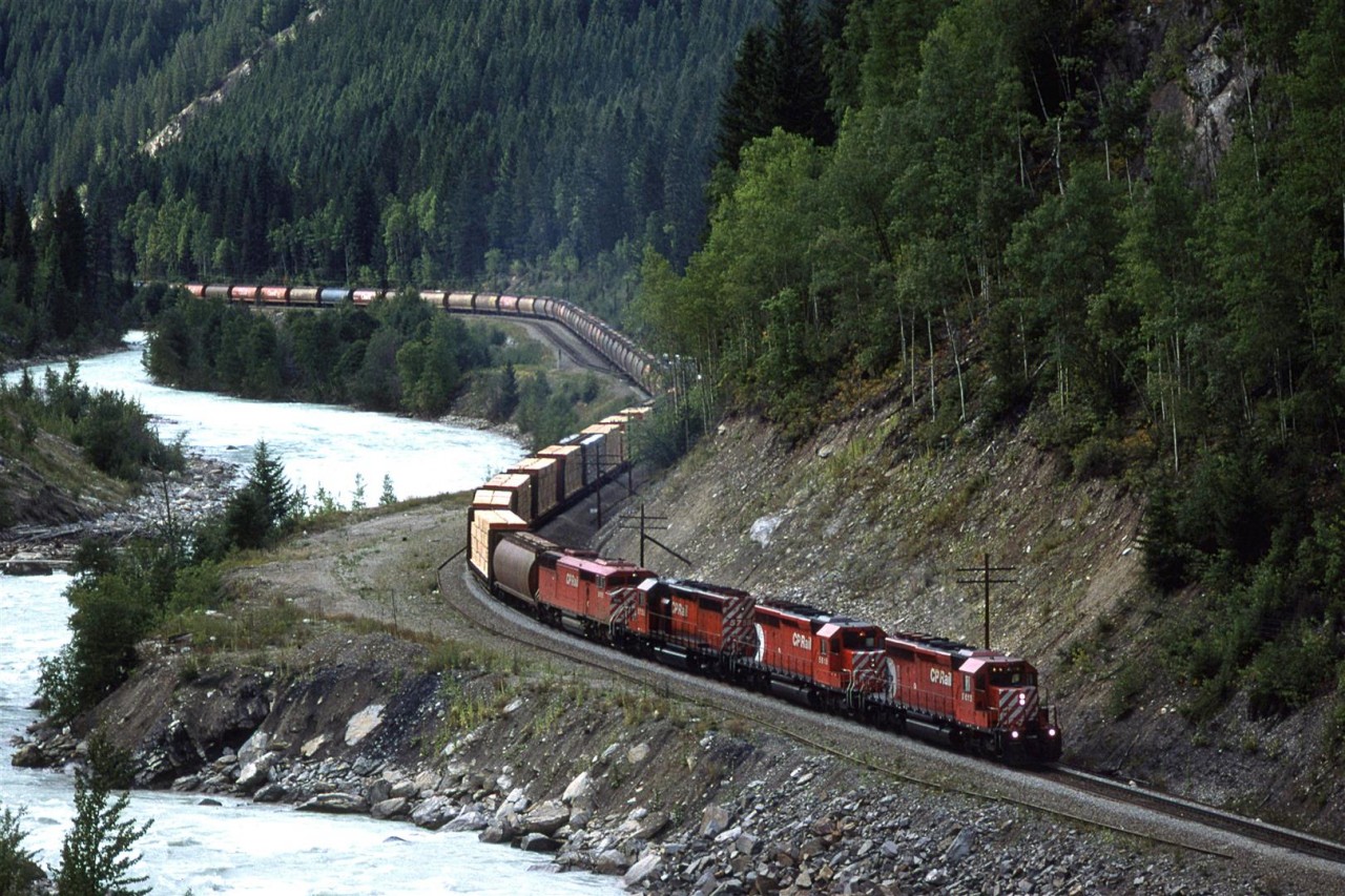 It sure looked to an outsider that CP would just throw together whatever was in the yard when they were assembling trains. When they enough to fill out the weight limit, they went, or if a train was a little light, they added a few more cars. Case in point; we have what looks to be an empty grain train (a lot lighter than when it arrived on the west coast), so why not stick on several heavy wood product cars?
I think that there is a pillar for the new high bridge on that point of land beside the wood product cars, therefore, we probably lose this view, but I suspect that the view from the bridge is rather good.