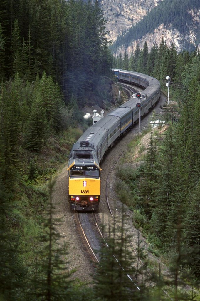 The eastbound "Canadian" is at the east end of Partridge siding, above both Spiral Tunnels in Kicking Horse Pass.
I had some difficulty identifying the exact photo location, because i could not figure out where I was on Google Maps. It was easy to find the east switch, but the track seemed to have a strange configuration. Well, after some more Googling, I learned that Partridge was extended eastward a few thousand feet sometime since this photo was taken.
This train is sporting what I would assume was the regular power contingent - a new F-40PH and an old FPB-9. Subsequent passenger trains that we would see over the next day or two would have a CP unit tacked on.