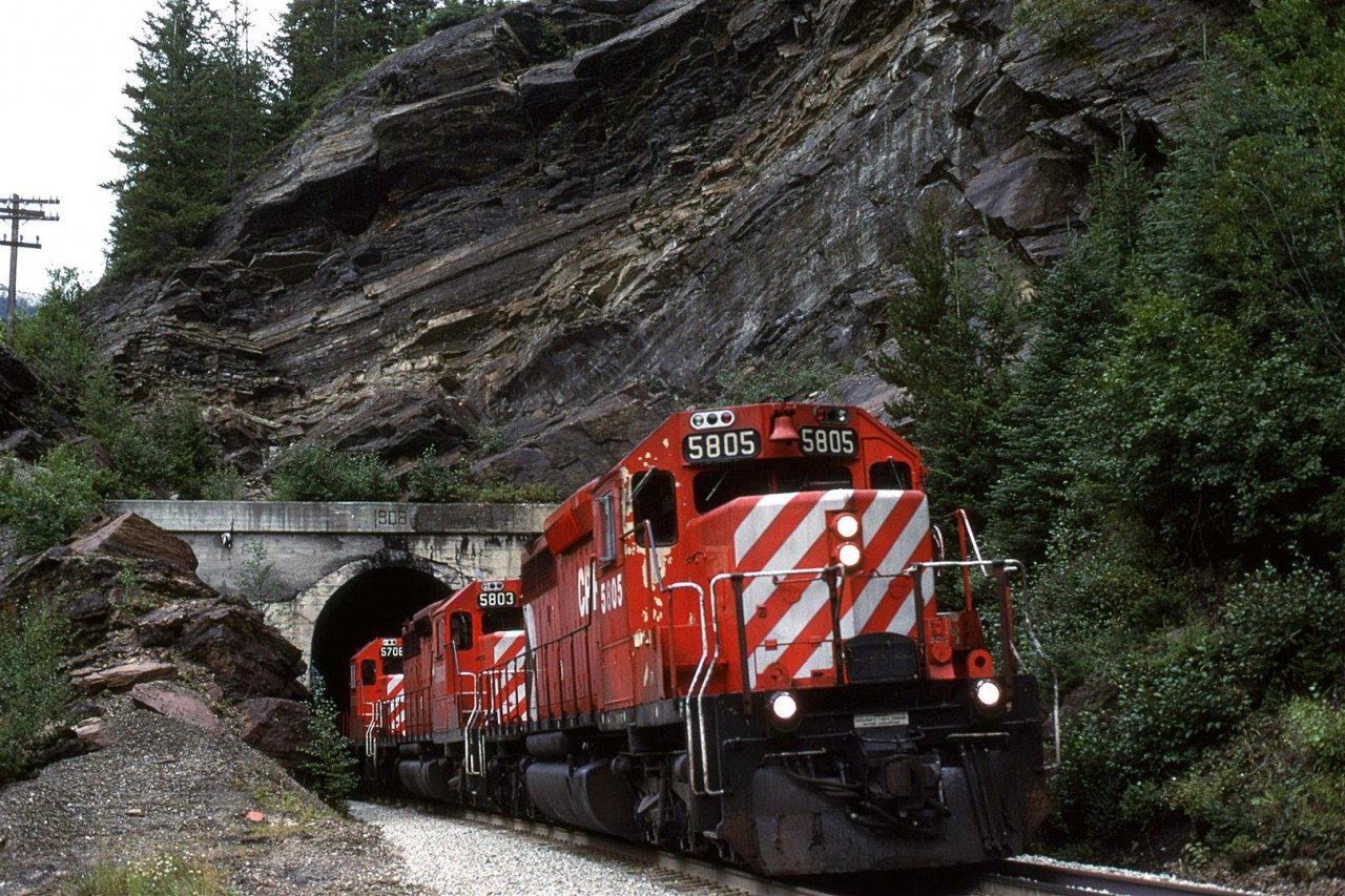 In order to show my railfan acquaintance how one can chase a train from the summit of Kicking Horse Pass all the way to Golden - the area covered by his planned guide, we decided to chase this train. The next several photos were all taken from roadside locations.
This was our fourth photo location, just west of the west switch of Cathedral. This short tunnel is adjacent to the highway. If you look carefully, you can see daylight trough the tunnel.From here to Field, the RR rides a shelf cut into the north side of Mount Stephen. There are a couple photo opportunities from the highway.