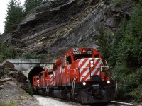 In order to show my railfan acquaintance how one can chase a train from the summit of Kicking Horse Pass all the way to Golden - the area covered by his planned guide, we decided to chase this train. The next several photos were all taken from roadside locations.
This was our fourth photo location, just west of the west switch of Cathedral. This short tunnel is adjacent to the highway. If you look carefully, you can see daylight trough the tunnel.From here to Field, the RR rides a shelf cut into the north side of Mount Stephen. There are a couple photo opportunities from the highway.