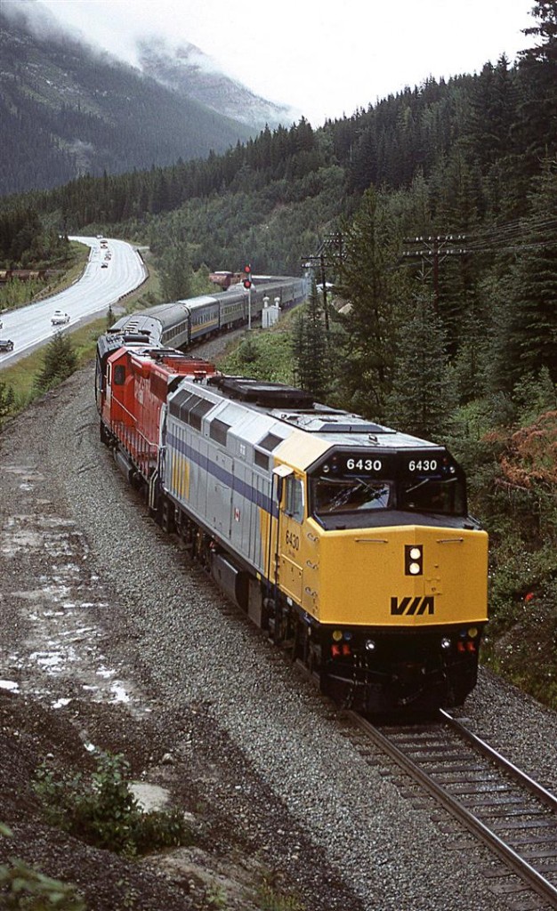 The westbound "Canadian" is about to enter the tiny tunnel just past the west switch of Cathedral Siding. Once again, there is a CP unit in the consist this day. Odd.
It may look like CP made a bargain with VIA - in exchange for the SD40, CP could tack on some grain hoppers. Well, that is not the case. There is an eastbound train in Cathedral Siding (The caboose may be seen above the prominent dome car.