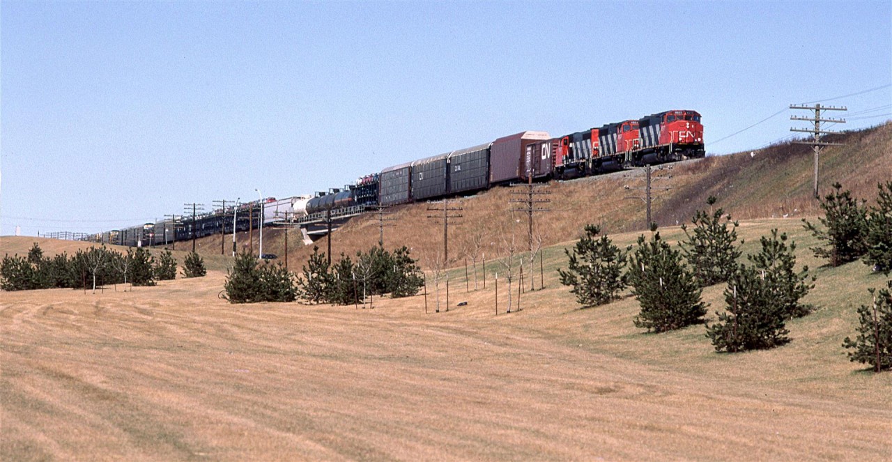 218 is close to arriving at east Edmonton's Clover Bar yard where CN likes to keep most of the hazardous materials, and where they have an automobile transfer yard. Both those types of loads are a dead giveaway that this is train #218.
It is seen on the embankment for the approach to the high bridge over the North Saskatchewan River.
Some of the efforts for Edmonton's beautification projects can be seen in the foreground.