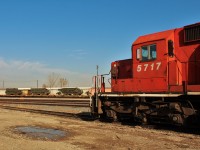 CP 5717 looks on as a train rolls through the yard with flatcar loads of military vehicles.