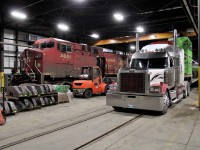 Four types of machinery are visible in this shop shot. AC4400 9651 is on the wheel truing machine while the Toyota forklift is parked between it and a semi truck making a delivery. At the left is a hand truck to move skids of GE gear cases around.