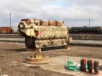 The EMD engine from CP 5824 sits on blocks with the flywheel and turbocharger end clearly visible. The turbo lubricating pump & motor is on the engine deck with it's piping leading to the blue oil filter. The larger orange filter is for the turbo. In the foreground is the magnet attachment for the CAT machine.