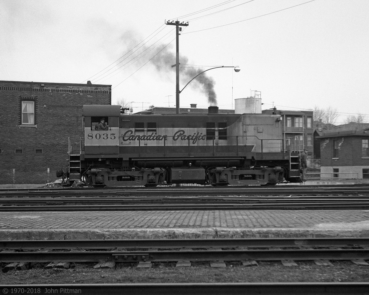 RS-23 CP 8035 has been switching the yard, it is photographed here moving towards the Trois-Rivieres roundhouse with a brakeman riding the front footboard.  The short building on the right was the yard office. 
I'd like to find an historic aerial view of T-R to see how round was that roundhouse; it had an outside turntable and radial tracks and dated from steam engine days.
While the CP station (my  vantage point) has been preserved, everything visible on the far side of the tracks has gone.  The background you'd see nowadays would be Quebec Autoroute 40 atop a high retaining wall. The yard is still active, part of the Quebec-Gatineau Railway.