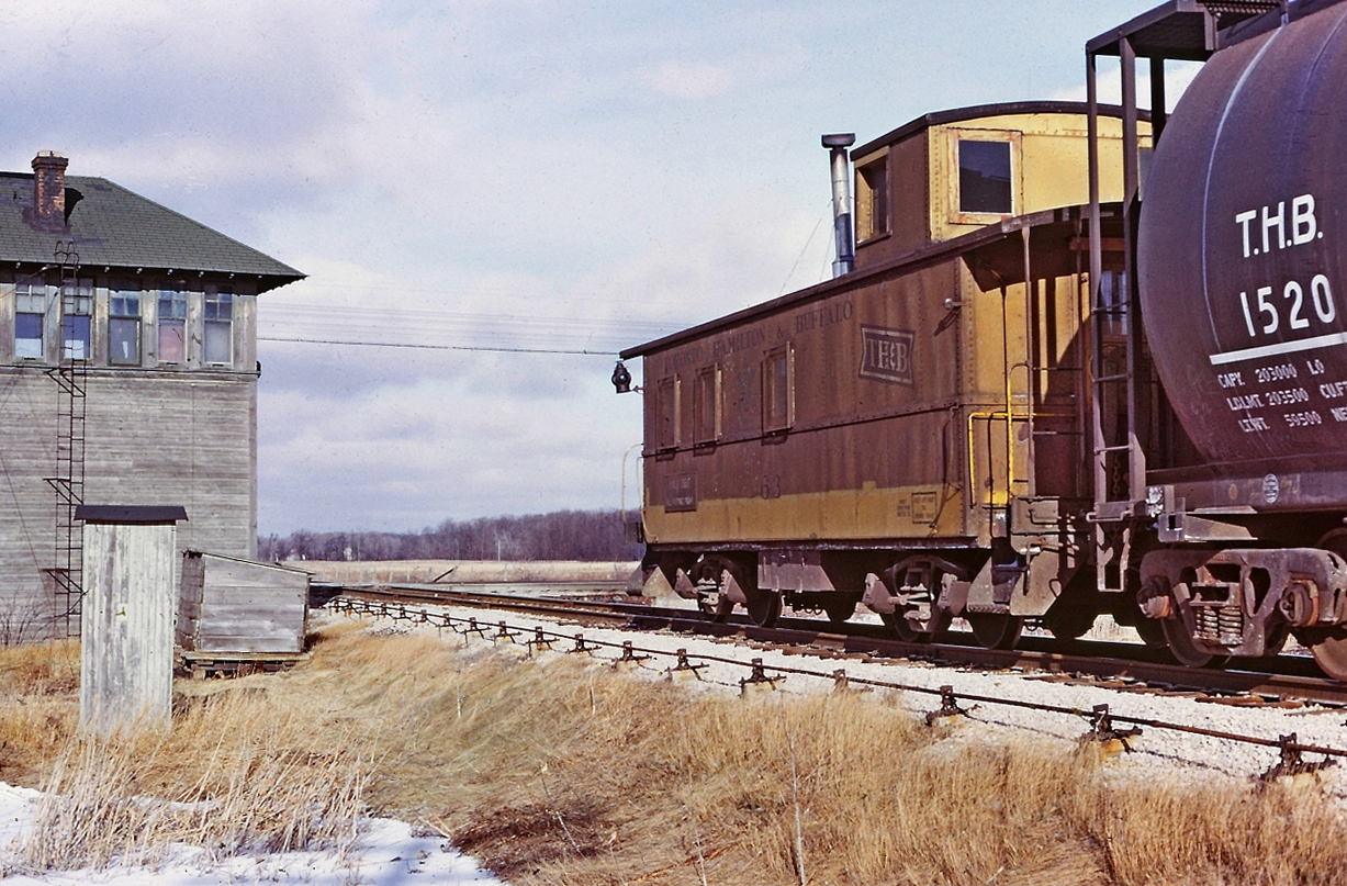 A Bruce Mercer image shows TH&B 63 caboose on the rear of the train, just
clearing the diamond at E&O Tower, southbound to Port Maitland.
 During my one plus year with the TH&B I did 12
trips on the East Local. We went on duty at Aberdeen yard mid-morning
around 9am. Usually it was a four person crew, Engineer, Conductor and
two Brakemen although sometimes we did have a Fireman, making a five man
crew. Trips varied in length from 8 hours to 12 hours or so. Departing
Aberdeen we would stop at Smithville and do some switching there and
then exit the Welland sub for the Dunnville sub and the 19 mile jaunt to
Port Maitland. Arriving at Port Maitland we would have a quick lunch
break and then start the heavy switching at the ERCO fertilizer plants.
We would eventually finish our work and building our train and then head
back to Smithville and eventually Aberdeen yard in Hamilton. Sometimes
we would take another break in Dunnville at the local greasy spoon
restaurant.