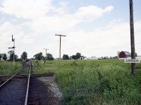 About halfway between Stirling and Hoards; maybe better posted as about 3 miles west of Stirling, lies this former diamond.  At this location the CN Campbellford Sub crosses the CN Marmora Sub, which is in this photo the line running Top to Bottom.  The location was but a crossing of the two routes, with a connector and siding on the northwest side; as one can see a gon on the connector and some MoW farther along. And a tool shed sort of building up by the road crossing, distant, on the right.
The location was referred to as Anson Jct by the railroaders from the old Central Ontario Railway that first put down the line thru here in 1883.
On the lower right where the sign is situated I believe is where a small frame building once stood, it was used by the crews during train operations when no one was on duty there. Too small to be a station so it was not much more than a railway operations point.  I'm wondering if the building in the distance is the same one that once stood on this spot.
Both lines were taken up in the mid 1980s. Not much to look at, but this location was once busy and significant to railroading in eastern Ontario.