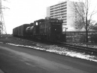 Dismal grey December day, but historical image. This view is of CN 1227 running eastward to CN Oakville sub where the old Beach line joins up at Burlington West. The end of the train is about to clear Lakeshore Rd and behind me is the crossing on Brock St.  The train is returning from switching out cars at businesses at the end of the line down by Langs Food Ltd. Before the Stoney Creek traffic circle was removed in the early 70s and the QEW thru there rebuilt, the CN line extended another 0.8 mile past Langs and joined the CN Grimsby sub in Stoney Creek, near Lake Av. My recollection of the former Beach Sub is a bit fuzzy. I believe service ended in 1977, track abandoned in 1981 and pulled up in 1983. The location of this photo can be identified by the white apartment which is still standing at the corner of Lakeshore Rd and Maple Av. In the left background was where the 'famous' Brant Inn stood until about 5 years before this photo was taken. The area is all built up now.