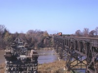 This is pretty well just an image to kindle the curiosity of those who enjoy history in Niagara. The image shows the two bridge structures over the Jordan Harbour/Twenty Mile Creek, part of the CN Grimsby sub.
It is my understanding that the first bridge, built around 1853, was wooden. But cannot verify this. (Great Western line between Hamilton and Niagara Falls opened in November 1853) The stone pillars you see on the left supported the railroad bridge built in 1867 and it remained in service until around 1900-1903; when the current bridge was built and opened for traffic. To this day it remains in use.
The structures are best viewed from down on the water, but failing that, I shot this from the east side support which is still in place, but now very difficult to access to this photo spot due to extreme foliage. There is not all that much information out there on these structures, which I find rather frustrating. Something worth looking into.  The approaching train has CN 2511 and a couple of GP9s for power, heading to Fort Erie.