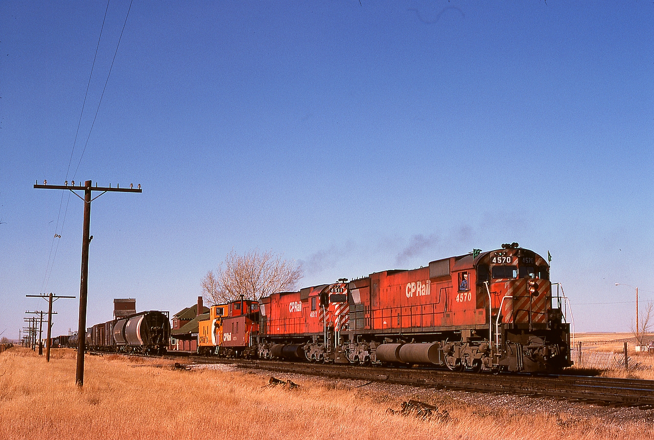 Coalhurst, west of Lethbridge, once was a simple junction of the Aldersyde and Turin subs from the north with the west-east Crowsnest sub., and as such had a small yard and a 24/7 train order office in the depot as shown here beyond the tail end of First 992 (note the green flags) with a pair of M-630s on Wednesday 1974-10-16.  They have just set off the train they brought down from Alyth in Calgary and are headed to Lethbridge.

Nowadays, Kipp yard and maintenance facility occupy the space west and north of this location, replacing the downtown Lethbridge yard and roundhouse area which now has just the relocated through mainline and industrial trackage.