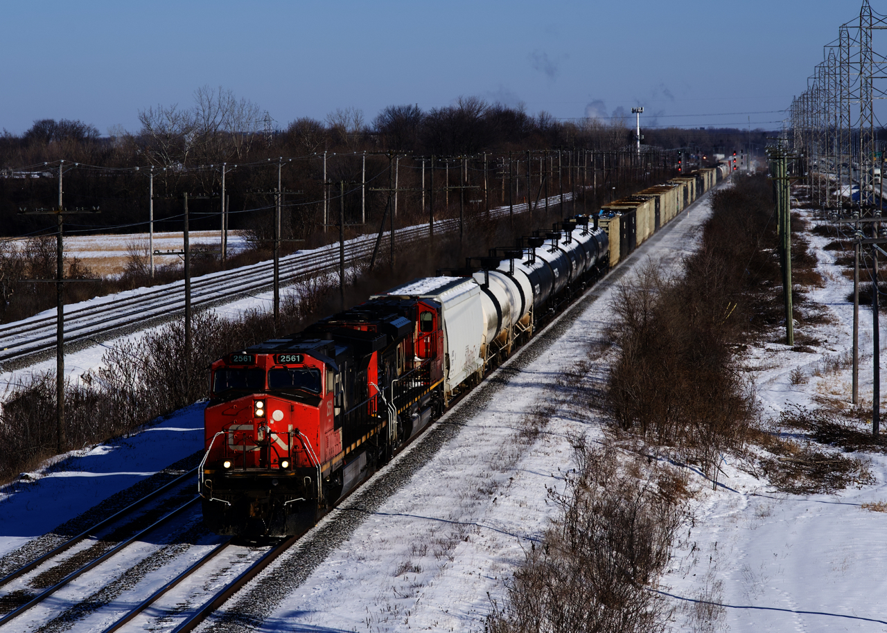 CN 369 heads west with CN 2561, CN 8875 and 124 cars on a frigid winter day. In the distance, counterpart CN 368 is lined on the north track and beyond that, the headlight of CP F95 is barely visible.