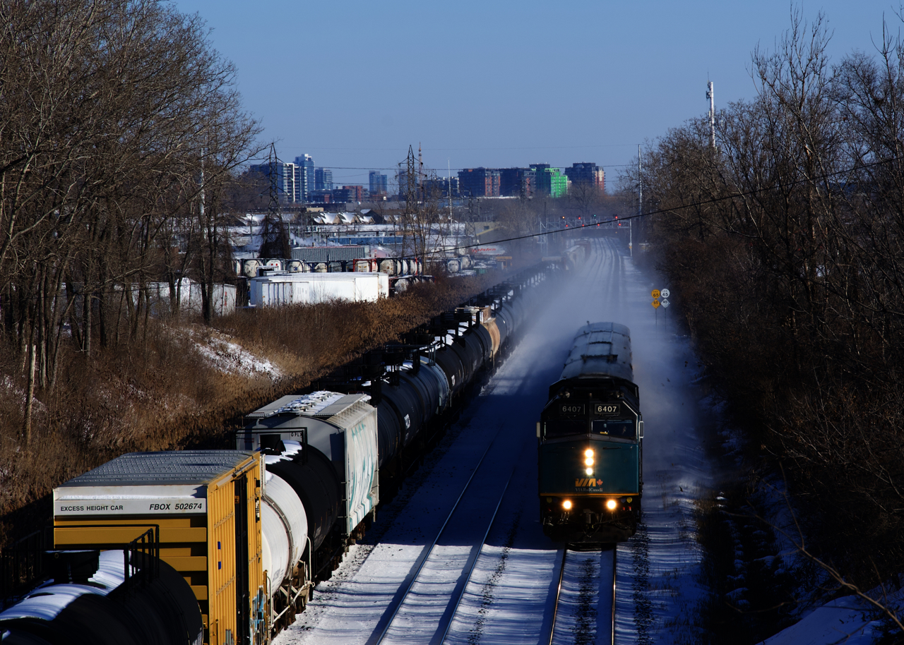 VIA 67 is kicking up snow as it passes some cars parked on the Freight Track of CN's Montreal Sub.