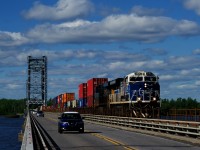 CN 327 with CSXT 3194 in the lead (with its white and blue nose) is being passed by a blue and white Nissan as both cross the Beauharnois canal on the Larocque Bridge.