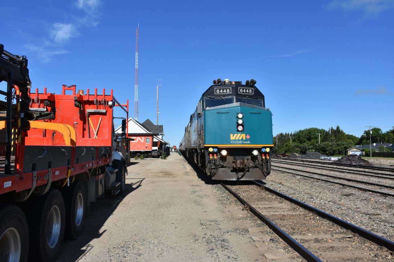 While VIA 692 lead by VIA 6448 sitting on the bolted rail mainline at Canora, SK commands the center of attention in this photo, there is so much more going on all around the shot. Off to the right of the locomotive are piles of new track material (spikes, anchors, tie plates) suggesting some major track work is in the works. To the left is a 2000 model year Freightliner 114 SD CN hi-rail boom truck (CN 270195) with tie grapple, a retired CN transfer van (CN 76659) on display at the historic 1904 built Canora station, a green flag signaling the end of a slow order on the line, a couple of communication towers with antennas pointing skyward, a few passengers milling about, a VIA on board service person manning the step box near the end of the train, and in the distance, sitting quietly in the yard waiting its next assignment is CN 5626. This 118 year old station got its name from a shortened Canadian Northern Railway .... CaNoRa. The building is now a visitor information center, museum, and VIA Rail station stop. Another beauty day for train travel and taking photos. ????