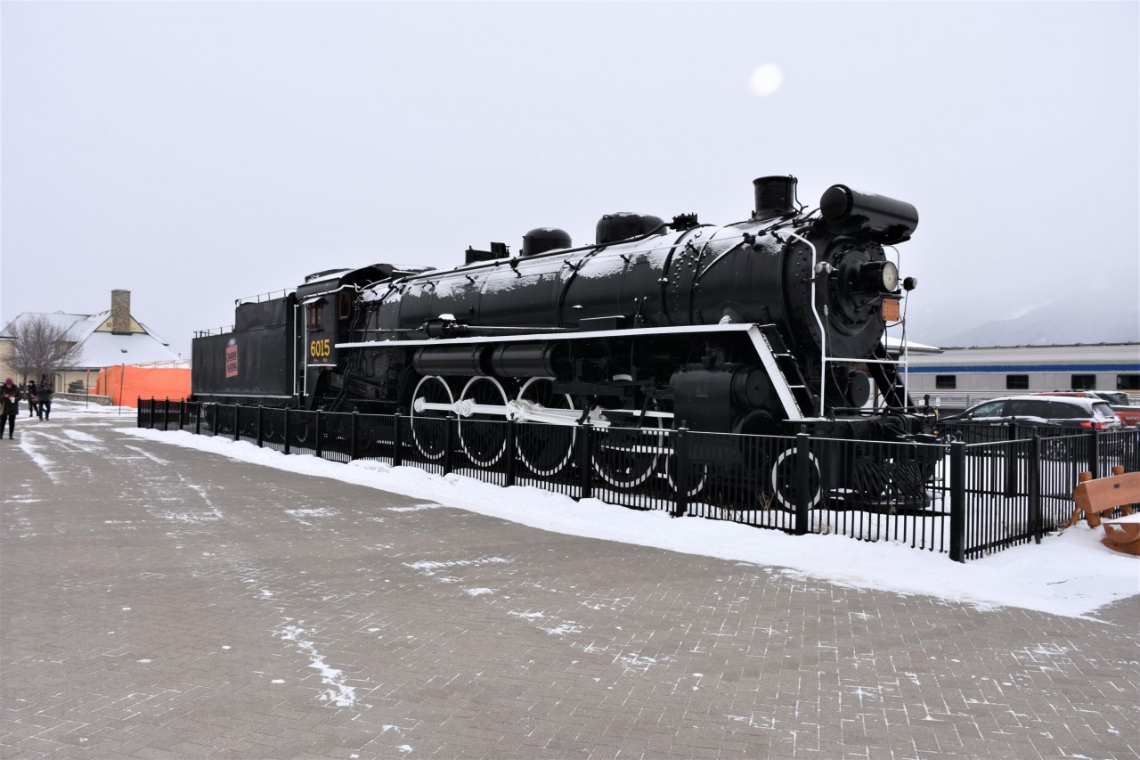 CNR's first batch of sixteen 4-8-2 Mountain types were delivered in 1923, were designated as Class U-1-a, and assigned road numbers 6000 through 6015. These steam locomotives had 26 x 30 cylinders, 73" drivers, a 210 psi boiler pressure, and exerted 49,588 lbs. of tractive effort. They weighed in at 354,110 lbs. and were used on express passenger trains between Montreal and Toronto.
Here we see CN 6015 Mountain type, but we don't see the mountains in Jasper, AB on this cold, windy, overcast, and snowy morning. The Jasper VIA station is at the left, and VIA #2 The Canadian is at the right of this magnificent steam locomotive.
For those in on the 'park bench' thing, there is one at the fence line in front of the locomotive. :-)