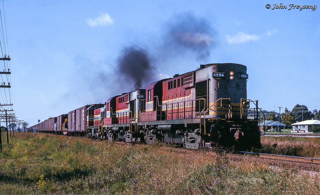 A pair of MLW RS10s lug an eastbound freight towards Smith Falls paralleling highway 2 though the hamlet of Smithfield, Ontario.  Trailing ALCO S2 7032 is in transit to Trenton where it will be assigned as the yard switcher.