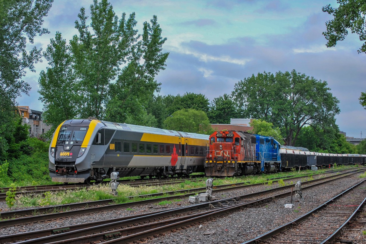 On June 13, 2023, VIA 37 (Quebec - Ottawa) has just left Central Station and entered the Montreal Subdivision. The train meets CN 596, the Pointe-Saint-Charles switcher, working a new gondola train.