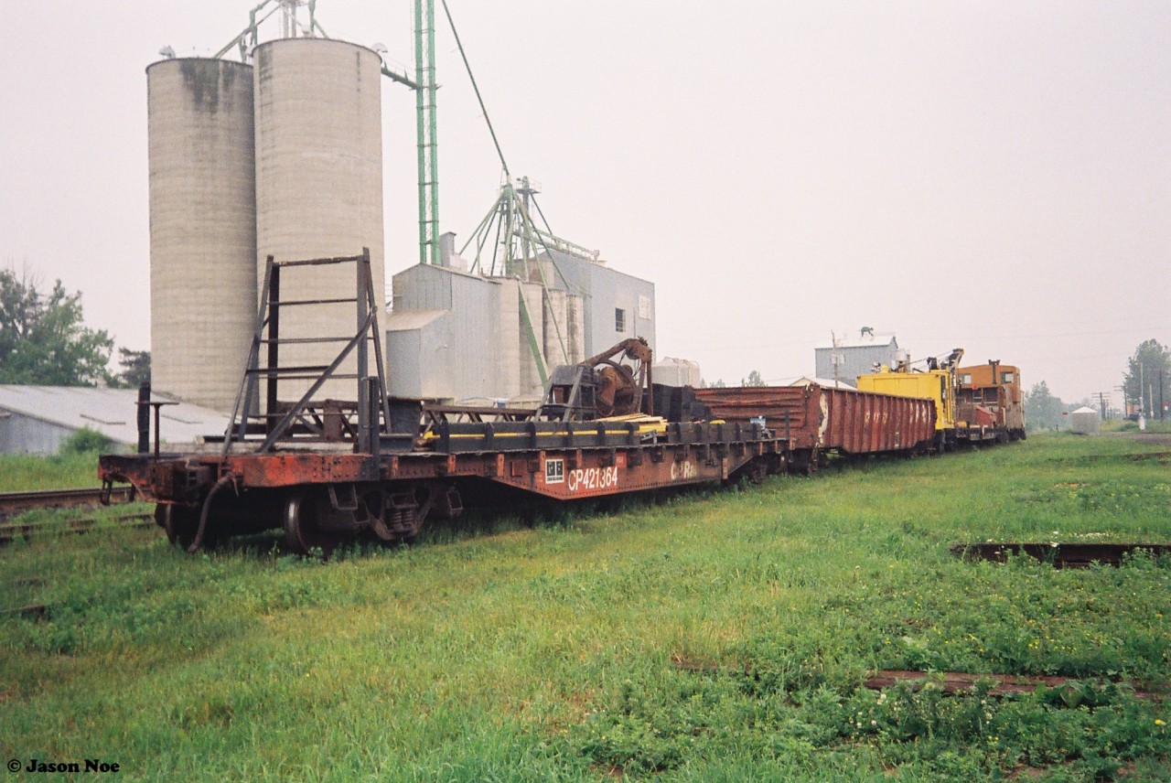 During a hazy summer afternoon, CP work equipment is seen in the town of Ayr, Ontario on the Galt Subdivision. The equipment includes flat car 421364, a gondola, a crane as well as CP caboose 434501. June 20, 1993.