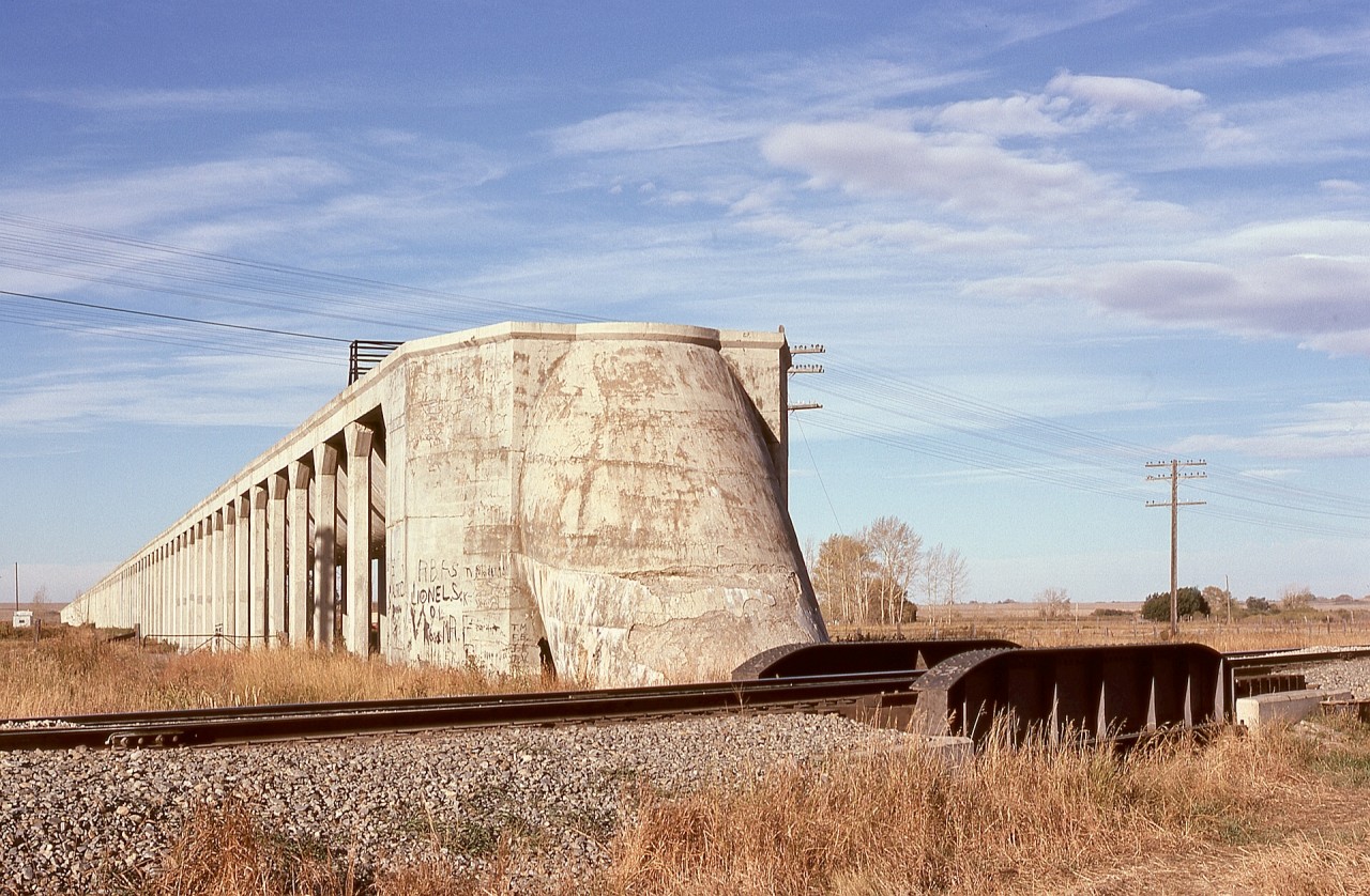 When an agricultural irrigation system utilizing water from Lake Newell was built by Canadian Pacific Railway in 1914, hoping to attract farmers to become settlers, the canal had an aqueduct portion of 1.9 miles to cross one low area, and that intersected the CP mainline a few miles east of Brooks.  To manage that crossing, an inverted siphon passed under the track at mileage 63.20 and the water continued northward to supply the rest of the system.  Check https://maps.app.goo.gl/fhep8hRtVhMANTXL8?g_st=im for an overview, and for more detail, see https://en.m.wikipedia.org/wiki/Brooks_Aqueduct.

This photo shows the siphon on Wednesday 1974-10-02.  But for wanting to photograph No. 1 expected on time 60 miles away at end-of-double-track at Gleichen (http://www.railpictures.ca/?attachment_id=50183), a shot of a train passing the siphon would have been ideal.

That arrangement of aqueduct and siphon was replaced in 1979 by a canal at a slightly lower level in an earthen berm, with a simpler culvert underpass of the railway a short distance east of the siphon at mileage 63.16, with the siphon and portions of the aqueduct now a National Historic Site.