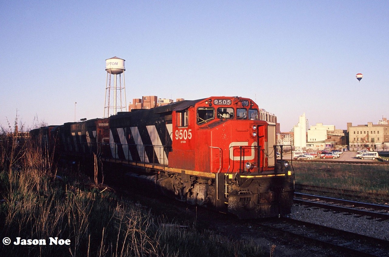 During a spring evening after completing their work, CN 421’s crew had to wait for the 15:30 Kitchener Job to return to the yard with their lift of newly built automotive frames from the Budd plant in Kitchener. Knowing they had some ample time to wait, they departed the yard light power down the siding towards King Street for some dinner options. The units included; CN GP40-2L(W) 9505, C-630M 2038 and an SD40-2(W). The power crossed King Street and stopped behind the plaza, that featured a Tim Hortons, Subway and a McDonalds across the street. At the time the siding extended even further west towards Park Street, however this portion was rarely used as most trains exited it at King Street through the cross-overs. 

So pictured here is 421’s power in the siding with the iconic Epton factory and its water tower in the background. Also, several other factories can be observed, showing-off Kitchener’s once vibrant industrial past. To the right of 9505 is the Guelph Subdivision mainline with another small siding track and the very far track is the Huron Park Spur. Today this is the location of the GO Transit layover facility and the plaza where the crew went that night is completely gone.