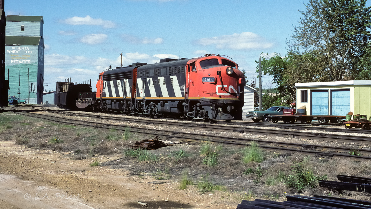 The fuel train was zipping right through town, no meet or stop on this day. A few interesting cars lead the 12+ tanks. 2 gondola loads of pipe for the oil field and a flat car of ties. Cab 79836 at the end, photo time 10:45.