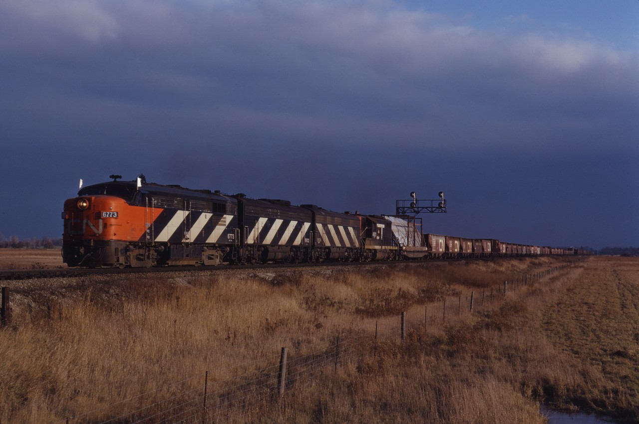 Under threatening skies, four passenger units (CN FPA4 6773, F9Bs 6632 and 6624, and borrowed GTW GP9 4921) move an eastbound train with a dimensional load through Milton as 1972 draws to a close.
