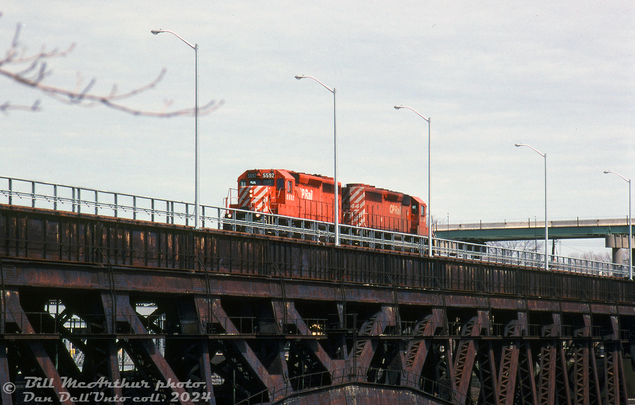 CP train #523 is a little light on cars today as CP SD40-2 units 5592 & 5644 lead it back into Canada from the US, crossing over the old Michigan Central Railway bridge into Niagara Falls, Ontario.

The center of the bridge would be Mile 0.0 "Niagara Falls" on CP's Hamilton Subdivions (the old Conrail Canada Division (PC/NYC/CASO/MCRR line) taken over by CN & CP in 1985). An agreement between CP and the city in 2001 would see trains stop running through town and the line ripped up through the downtown area, but due to the prohibitive cost of demolition, the old 1925-built bridge was just closed off and left to span the Niagara River in an abandoned state ever since.

Bill McArthur photo, Dan Dell'Unto collection slide.