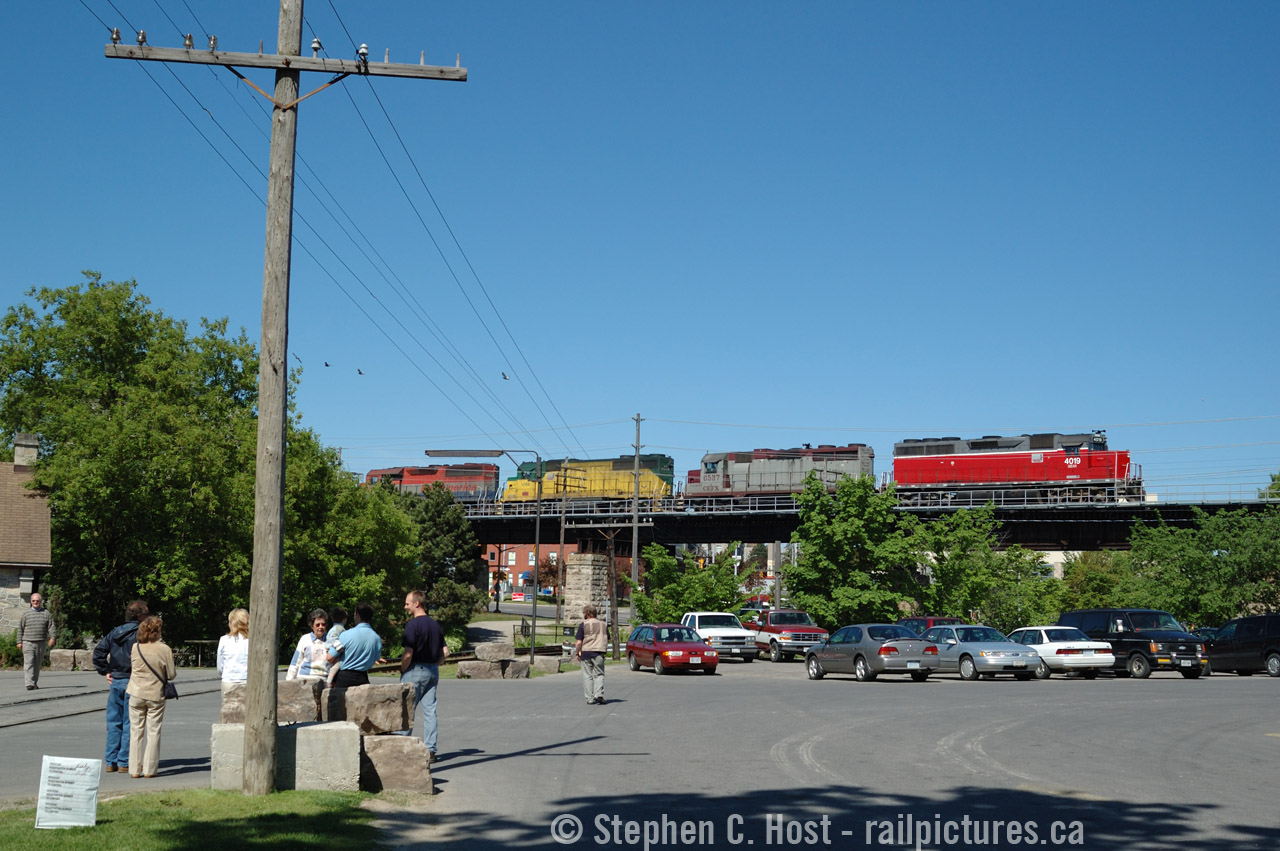 Visitors to an open house at WC Woods in Guelph mull around while a photographer for the Guelph Mercury in the vest looks at the train passing overhead. Hauling a d9r dimensional from Babcock and Wilcox (now BWXT) in Galt, this Extra 432 is heading east out of Guelph passing over downtown Guelph on a viaduct bridge built in the 1850's. This was the 'rainbow' era of GEXR where about 11-12 four axle units were all they had and big trains to/from Toronto with this classic power was a daily activity. The train is partially framed in the GJR 'telltale' that was located here until around 2019 when it was unceremoniously removed. This site has pretty much turned into condos now and will soon be a 5th building located where I am standing or thereabouts.