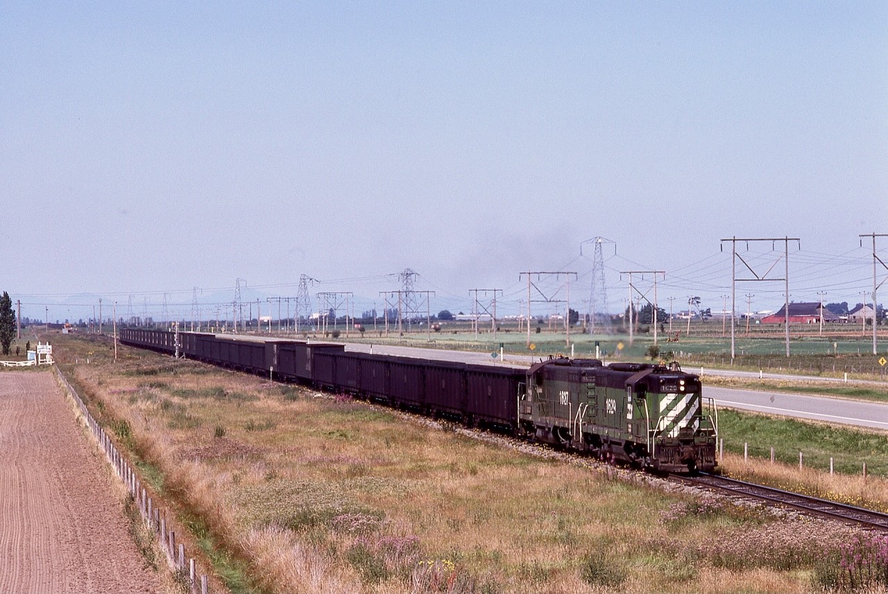 The Roberts Bank coal export terminal originally served just CP trains, then added CN traffic, then BN petroleum coke from Cherry Point refinery in Washington state.  Seen here, the New Westminster Local with a pair of BN GP9s, 1629 and 1627, is departing Gulf, about five miles from Roberts Bank, with empties, on Thursday 1979-07-19.