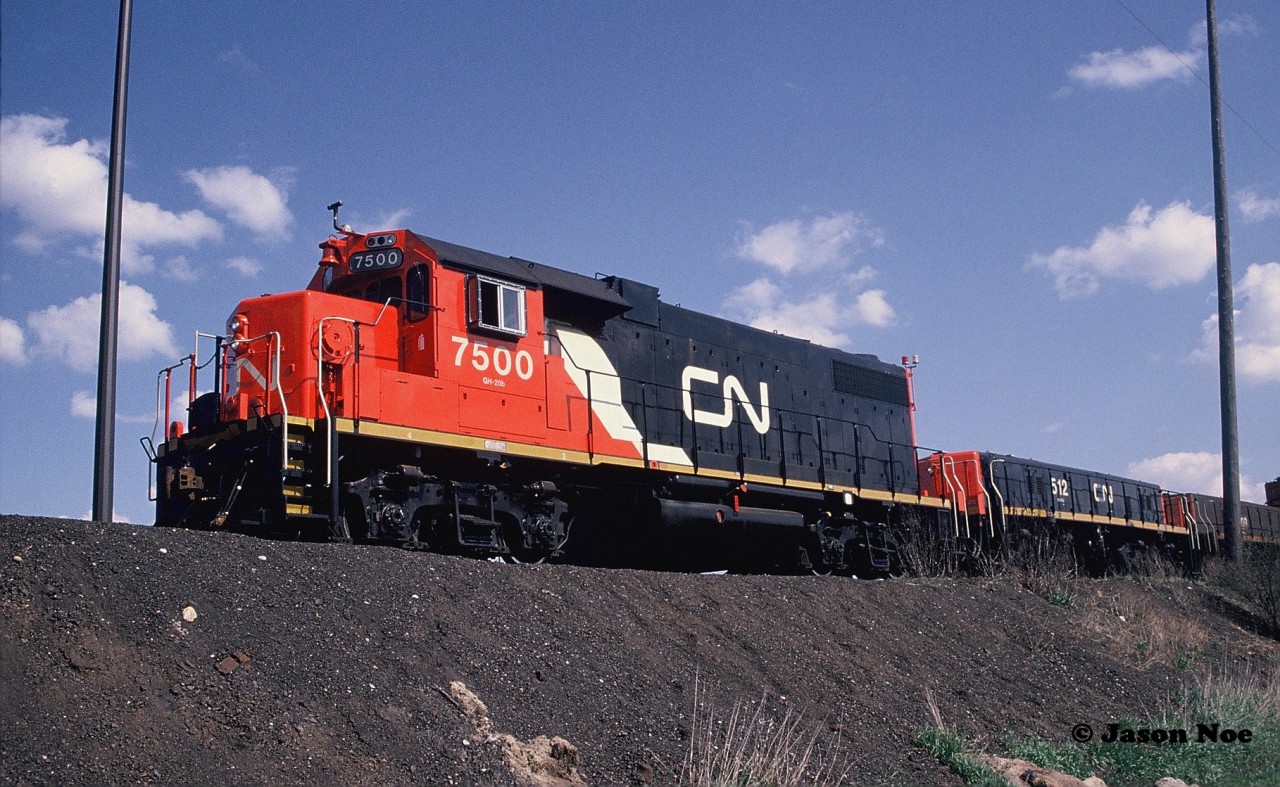 Freshly repaired and repainted CN GP38-2 7500 and YBU-4m yard slug 512 are viewed working the MacMillan Yard hump in Vaughn, Ontario with another set of power. The year prior both 7500 and 512 were involved in a derailment at MacMillan Yard and received extensive damage. One year later and both units were back working with 7500 adorned in the new CN livery that the company had applied to their four-axle units, minus the CNNA map. 
Here is a link below to a photo of wreck damaged 7500 taken by John Pittman in 1993.


www.railpictures.ca/?attachment_id=40681