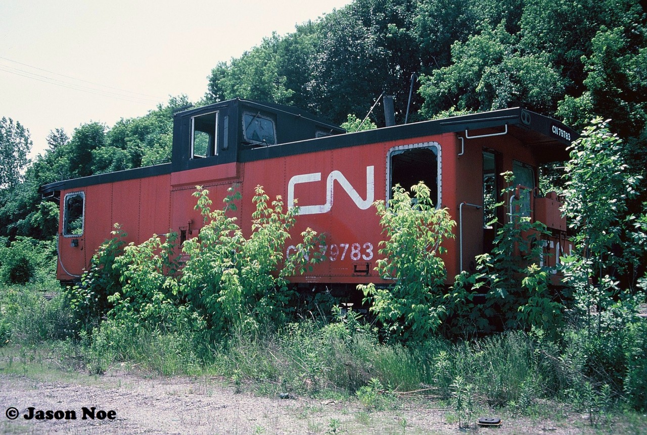 CN caboose 79783 sits amongst the ever-growing weeds and other brush at CN’s Stuart Street Yard in Hamilton, Ontario. This caboose and some other aging equipment had sat stored here behind the shop for many years.