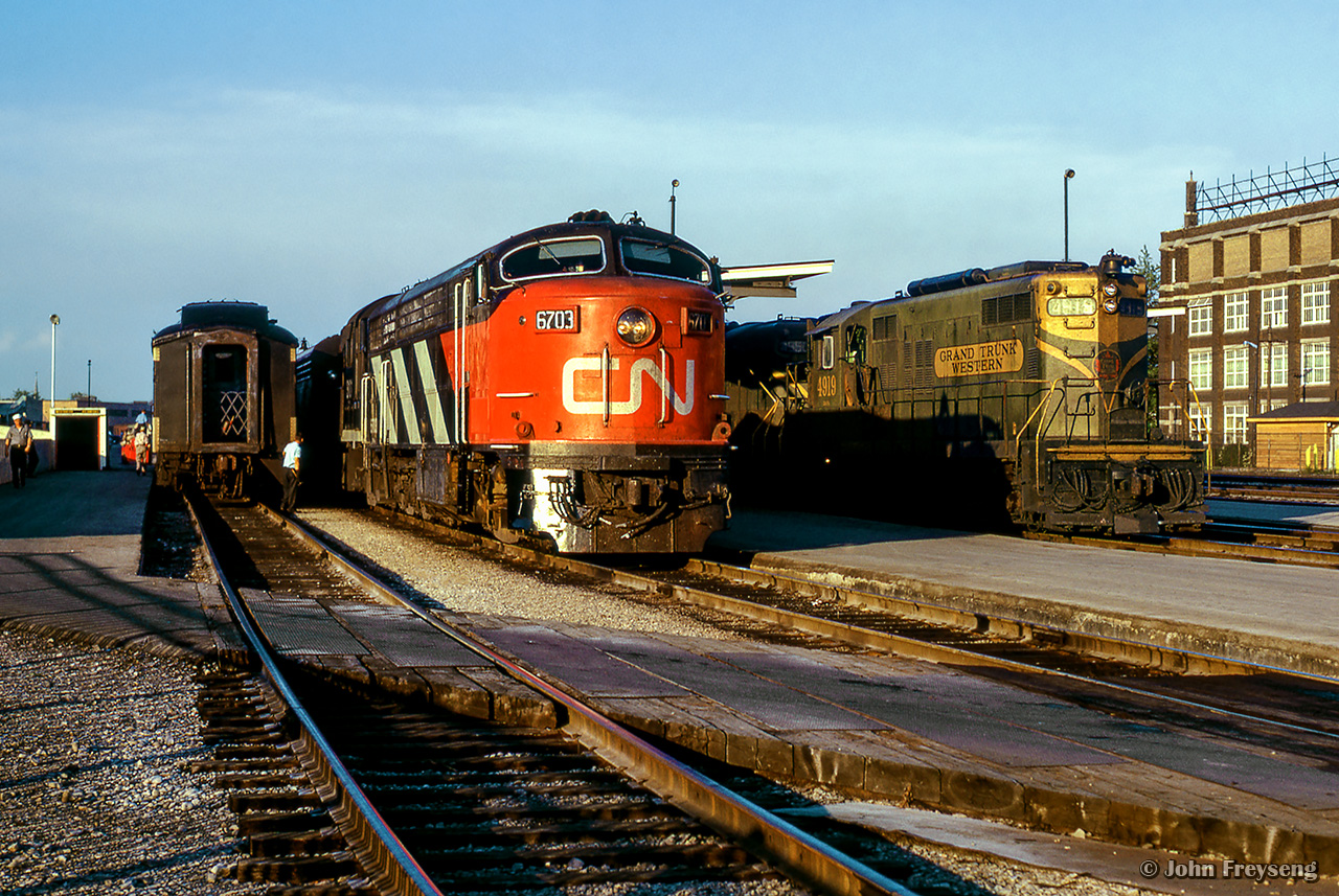 A sunny summer evening finds an assortment of power from three builders at the west end of London's passenger station.  At right is train 51, the Huron, from Toronto - Port Huron, Michigan via Kitchener, with a pair of EMD GP9s (4918/4950), while at left is train 41, the Erie, from Toronto - Windsor via Brantford, with a CLC CPA-16-5 (one of only six built), and an MLW RS18.  These CLC units were built with a five axle wheel arrangement, as seen better inDave Burrough's photo.



The time would be approximately 1918h if everything is on schedule, with 51 arriving at 1905h, and 41 arriving at 1915h, both trains will share the station for five minutes, when 51 will depart at 1920h, with 41 following towards Komoka at 1925h.



203 Bathurst Street can be seen off to the right.  Originally built as the Holeproof Hosiery Company in 1919, the company merged with the Julius Kayser Company in 1955, and was later sold to the Chester H. Roth Company in 1958, being renamed Kayser-Roth.  The company closed the factory in 1989, but the building still exists today as City Centre Storage.

Scan and editing by Jacob Patterson.