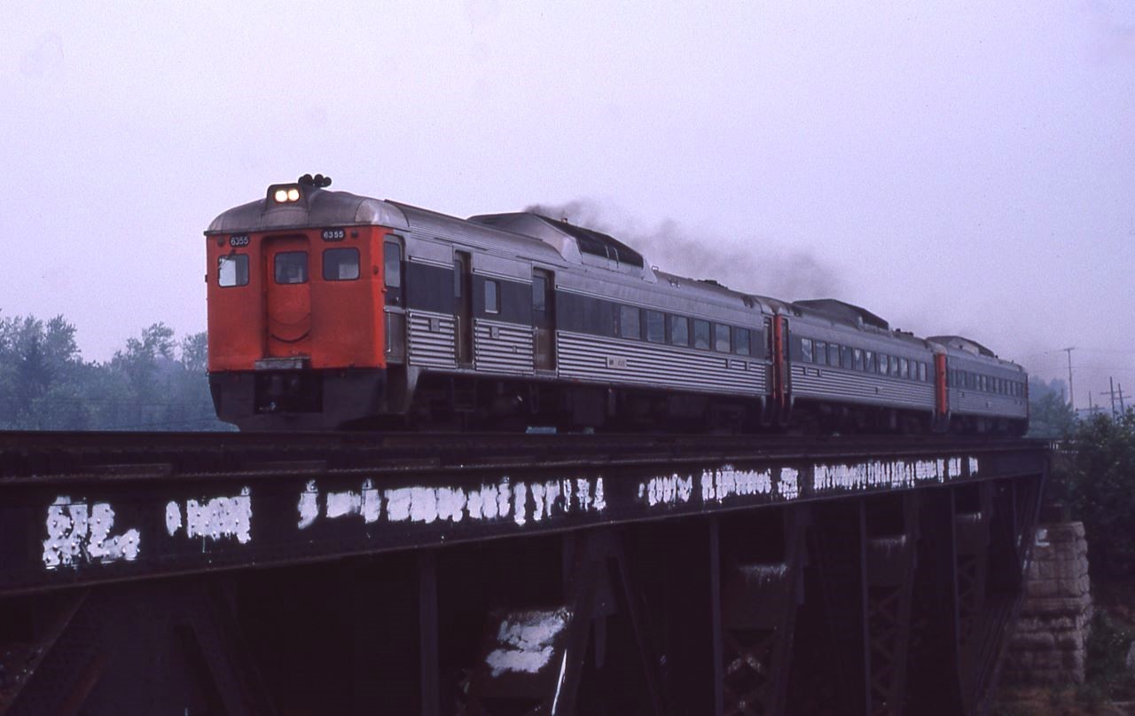 VIA train 637 screams across the Credit River bridge in Port Credit, Ontario on a very hot, humid, and smoggy July 20th, 1980 morning.  The three unit train consists of 6355, 6001, and 6122.