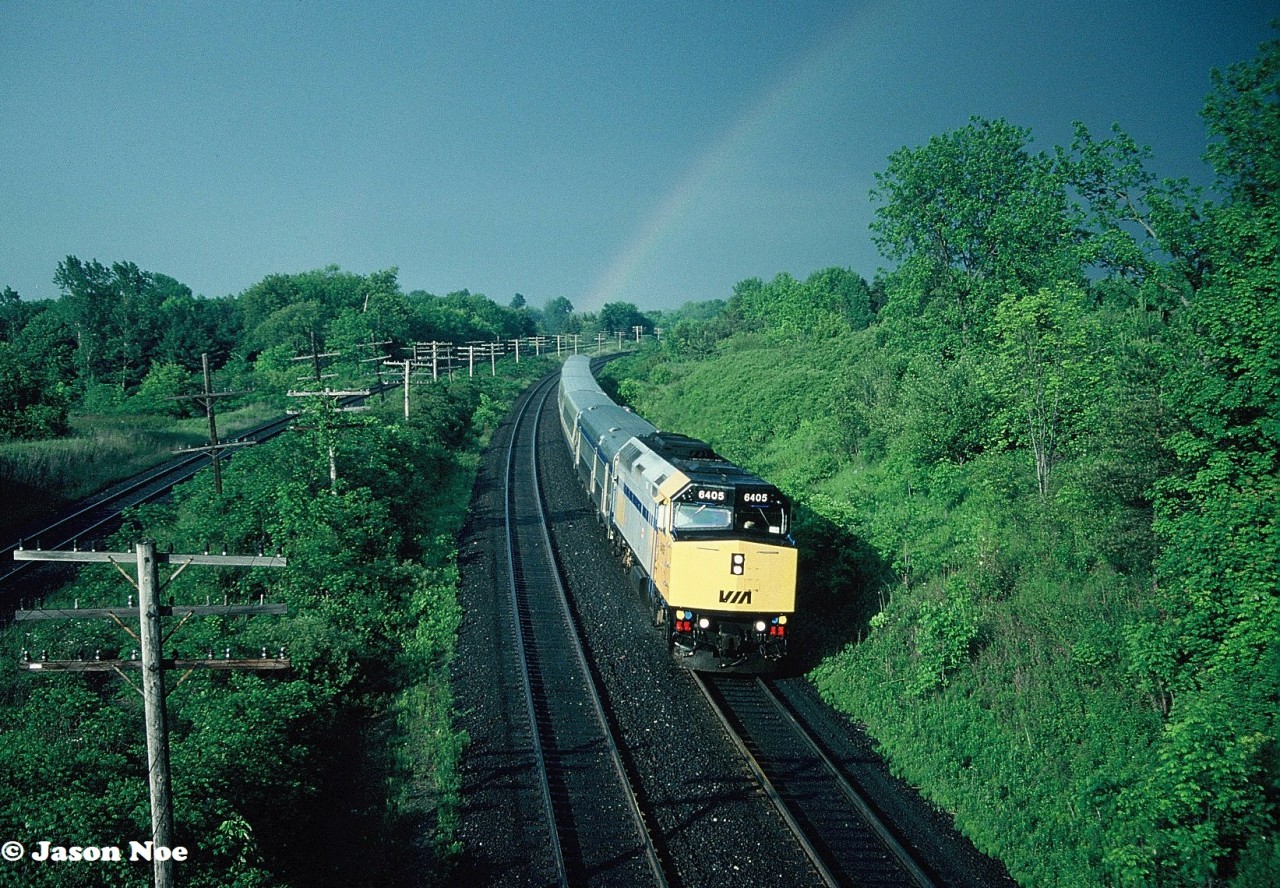 An evening thunderstorm has just cleared the Denfield Road bridge area at Hyde Park, Ontario and its remnants produced a rainbow over the CN Strathroy Subdivision as it continued to move into London. The timing was impeccable as VIA Rail #75 with 6405 is viewed rounding the curve approaching the bridge with several photographers there to capture the moment.