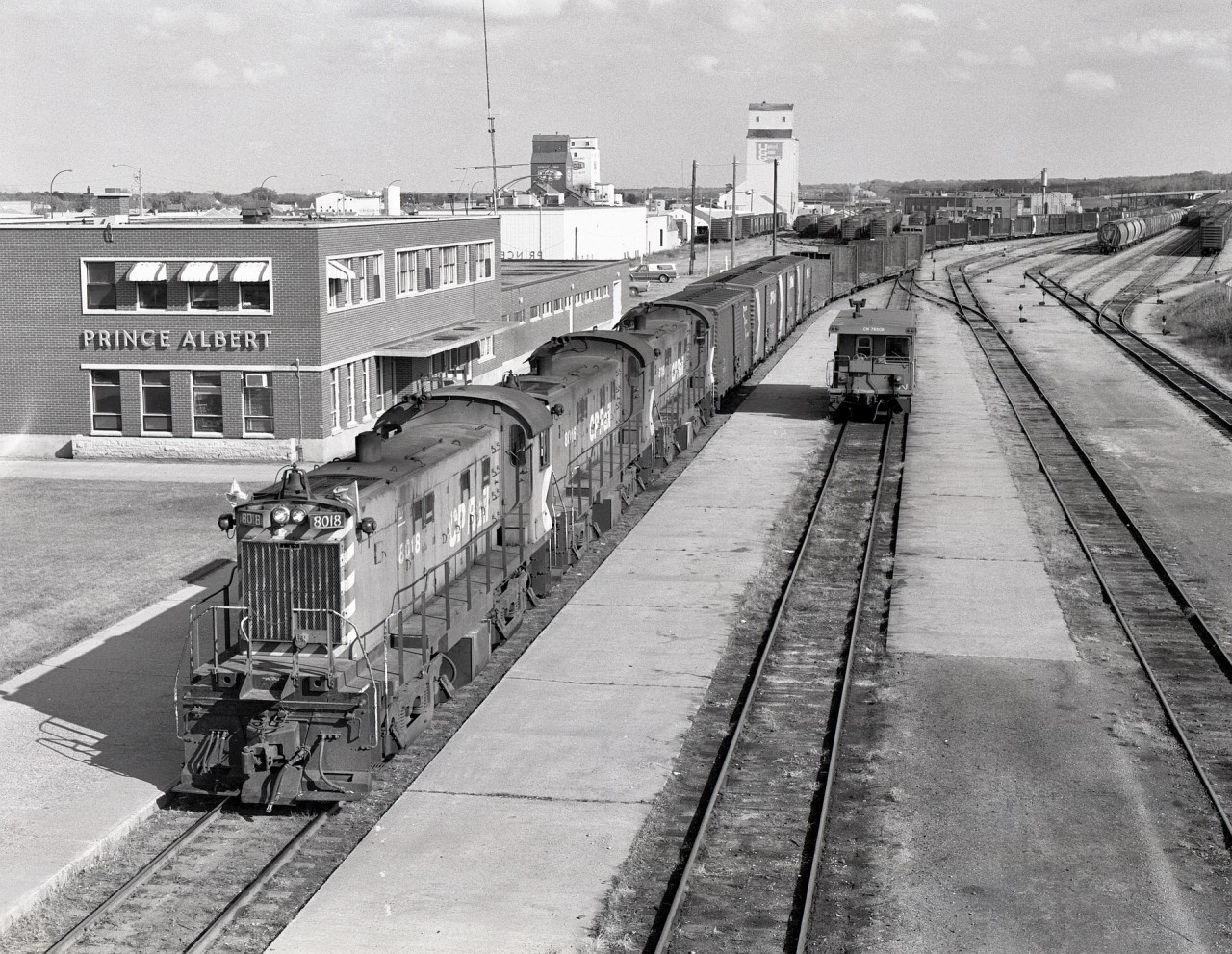 Viewed from the Central Avenue overpass in Prince Albert on Thursday 1981-09-24, with the headend on CN’s Duck Lake sub. and tailend still on CN’s Tisdale sub., this is CP’s freight westward to Meadow Lake.  This area was a spider’s web of CP running rights on numerous CN lines, and RS-23 lightweights CP 8018 + 8016 + 8015 have yet to navigate parts of the Blaine Lake and Big River subs. before reaching CP rails at Tobey near Debden.

Other than the CP yard in Prince Albert (parallel to and a couple blocks north of CN’s), the nearest CP tracks were Northway at 18.9 miles to the east, Sharpe at 18.2 miles to the north, and Tobey at 60.2 miles to the west.

Today, while the Prince Albert depot remains, much of the branchline network is history, and Carlton Trail Railway operates what remains.