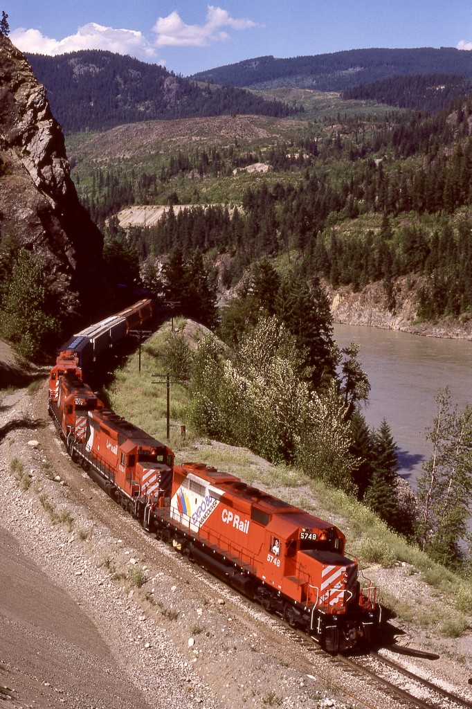 In the canyon of the Fraser River between Keefers and Chaumox, just a bit north of a bridge over the Nahatlatch River, a high and long gravel bank above a curve at mileage 113.5 provided a glorious elevated view of CP’s Thompson sub., and on Wednesday 1987-06-24 that perch was used to record a westward grain train with lead unit CP 5748 carrying Expo 86 markings and assisted by 5594 + 5772 + 5676.