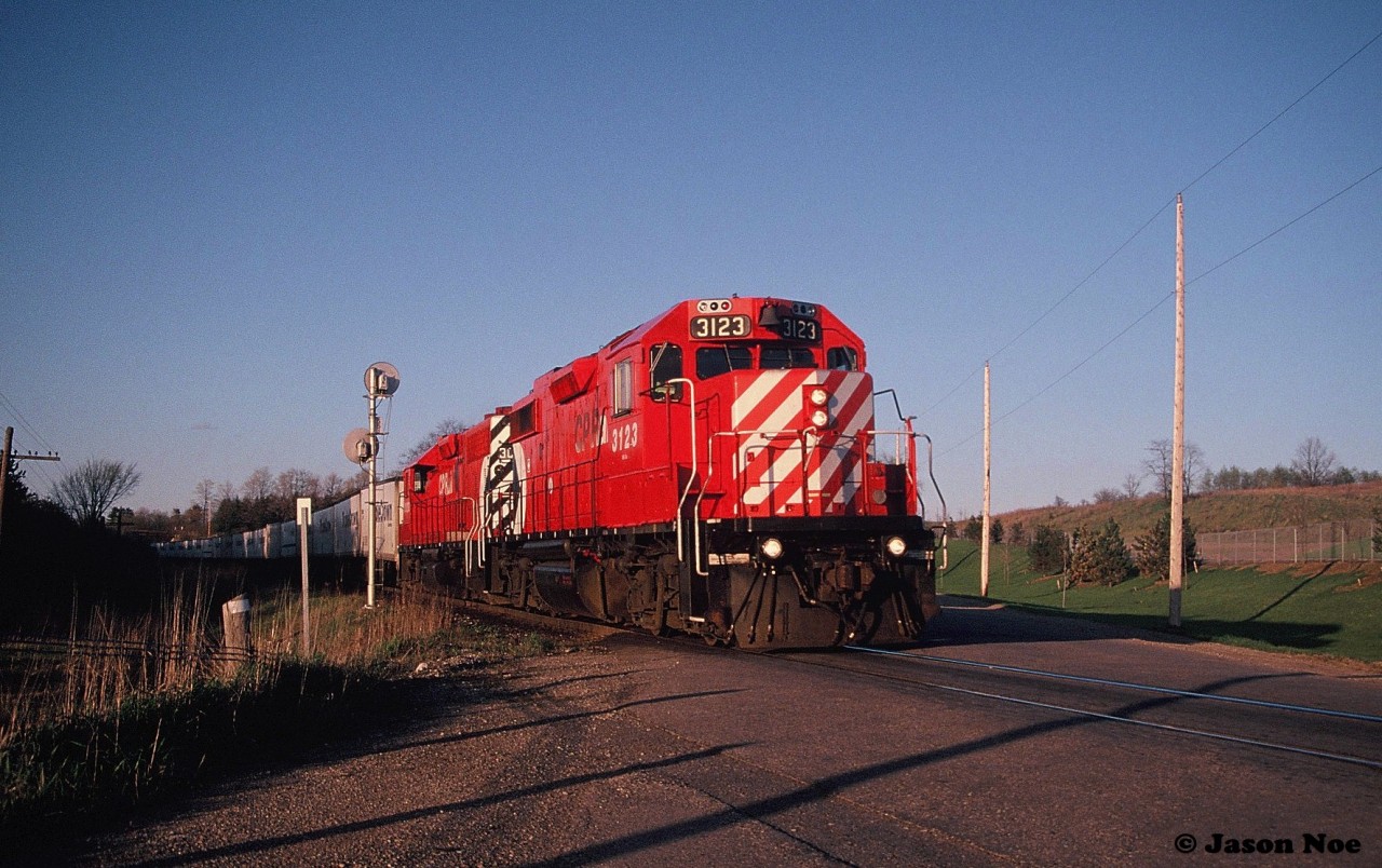 During a spring evening, the shadows are growing long as the westbound Road Railer (Train 529) with GP38-2 3123 leading is viewed crossing Clyde Road on the Galt Subdivision. The train is approaching the east siding switch at Killean, which at that time was still used regularly for meets.